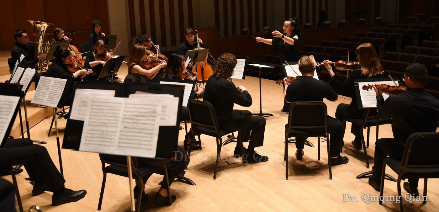 Dr. Qian leading an orchestra with musicians seated around her