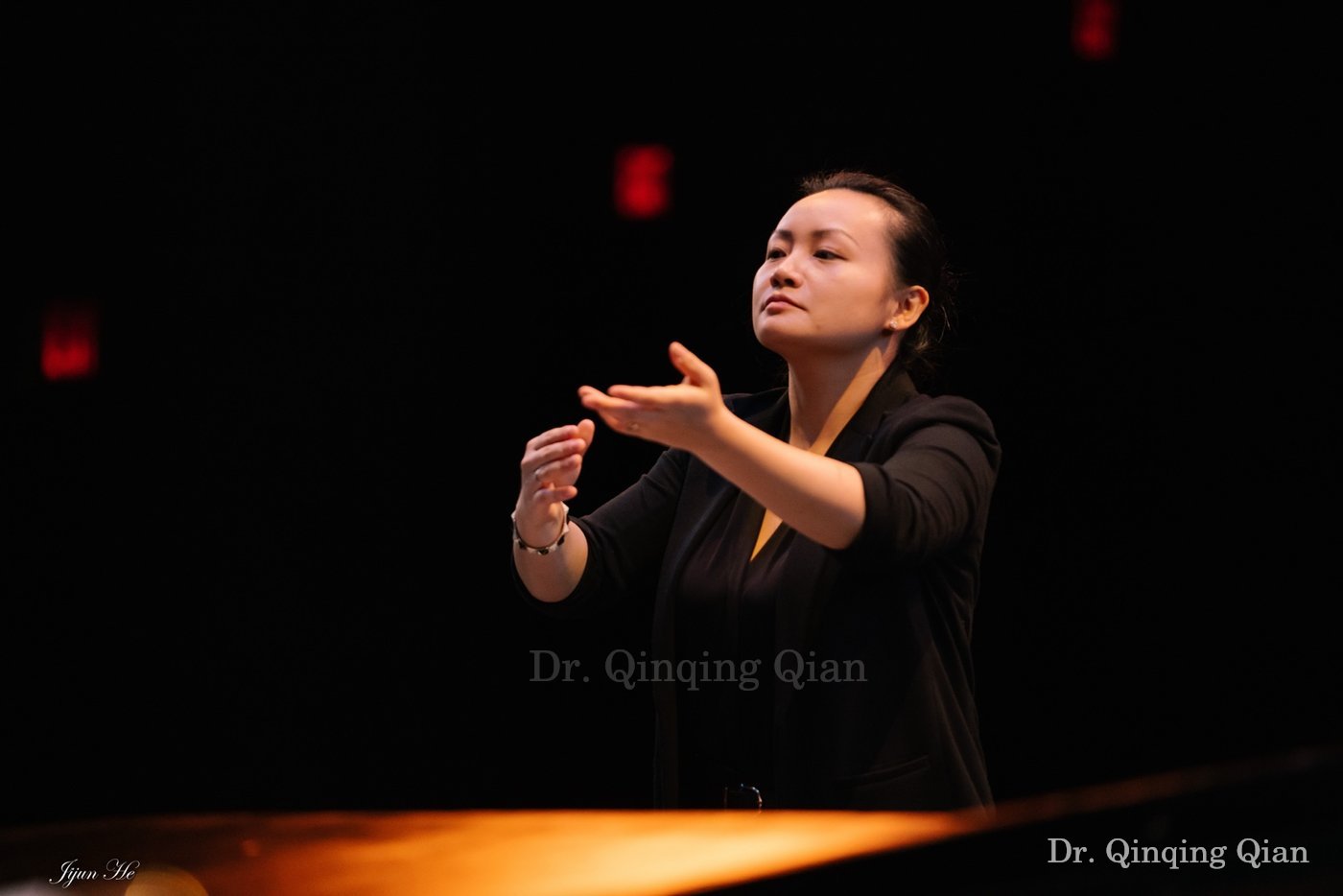 Dr. Qian conducting in formal concert dress on a darkened stage